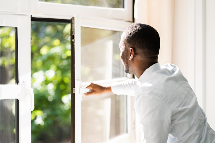 A man in a white shirt seen from behind, opening a window.