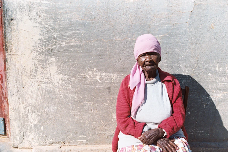 Khoe-San person sitting against cement wall.