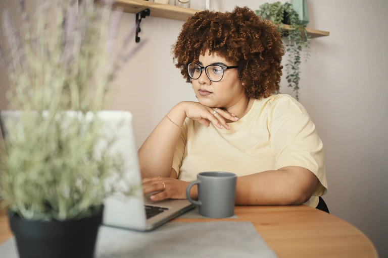 A woman looks on her computer, there's lavendar blurred in the foreground
