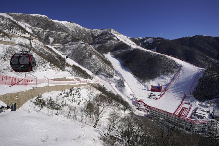 A gondola passes by with dark ground below and white ski slopes behind it.