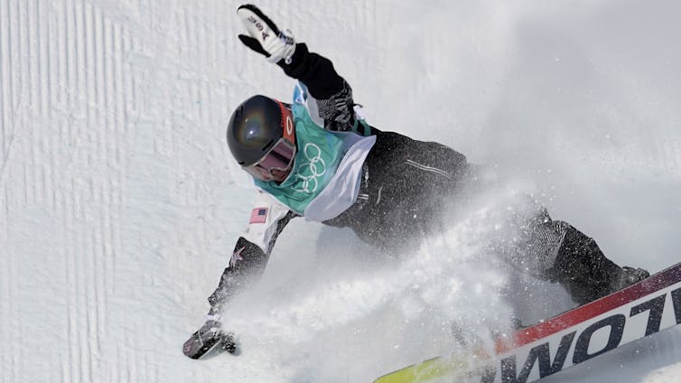 A snowboarder with 'USA' on her gloves puts her arms out for balance on a run.