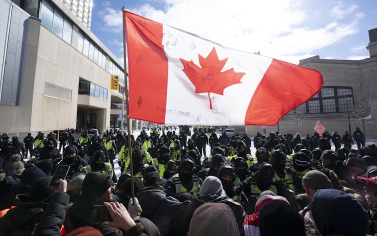 A Canada flag hangs over protesters and police.
