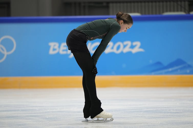 A skater on the ice, bent over with her hands on her knees