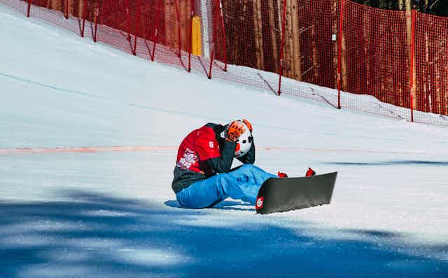 Une skieuse est assise dans la neige, tête entre les mains.