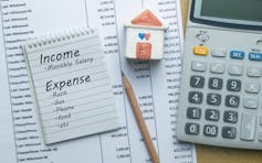 A list of household expenses and income is placed on top of a bill with a calculator beside it