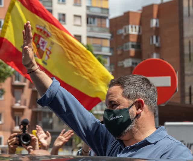 Santiago Abascal, líder de Vox, saludando con el brazo en alto ante una bandera de España y una señal de prohibido el paso.