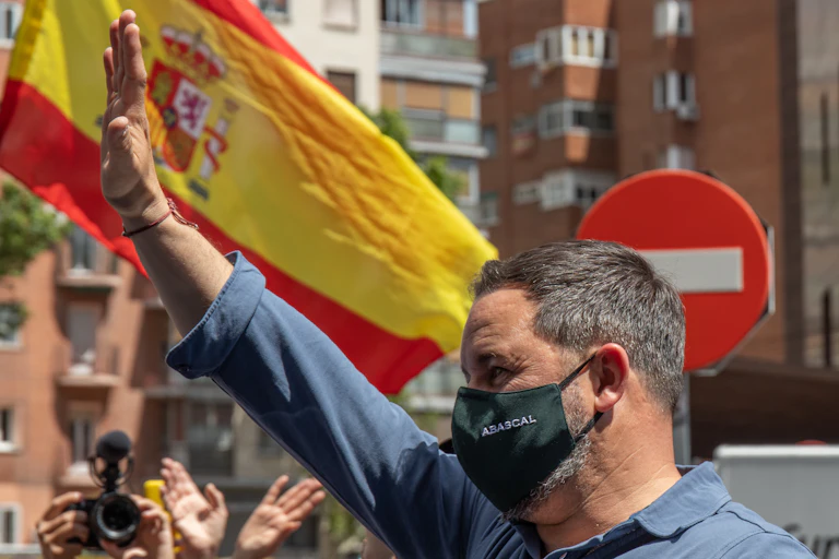 Santiago Abascal, líder de Vox, saludando con el brazo en alto ante una bandera de España y una señal de prohibido el paso.