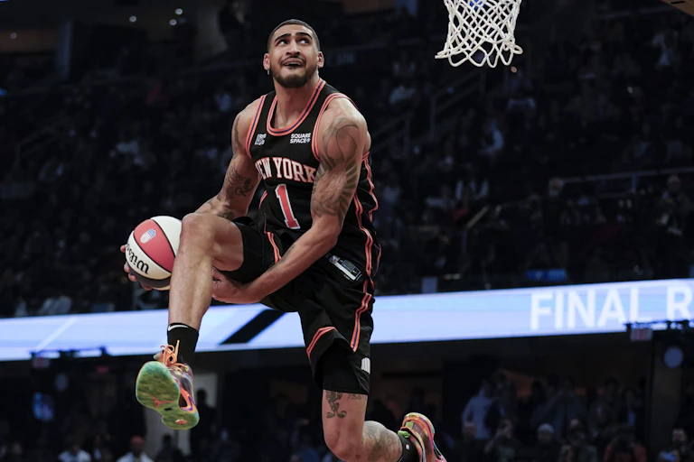 An airborne basketball player moves the ball through his legs as he goes up for a slam dunk.