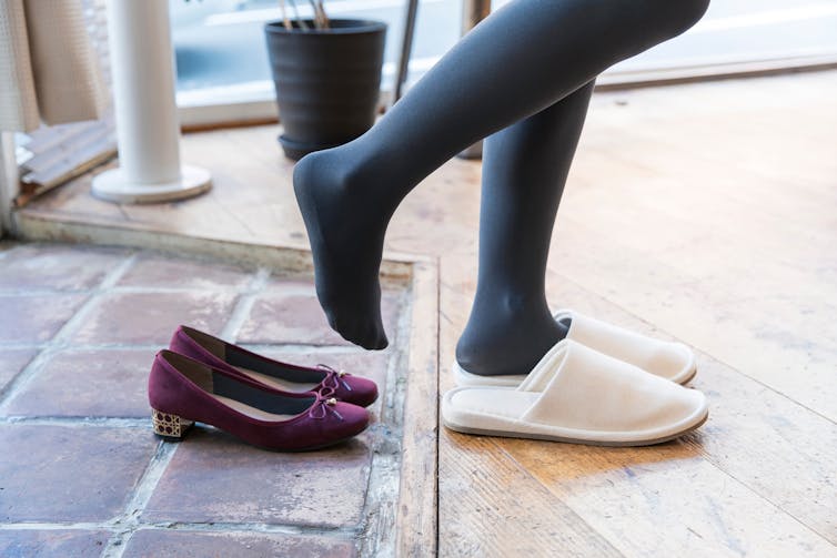 A woman removes shoes at the front door.