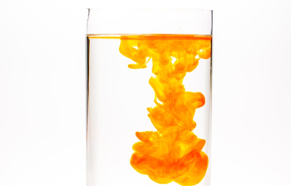 Orange food colouring or ink spreads in a glass of water, introducing colour to the plain liquid.