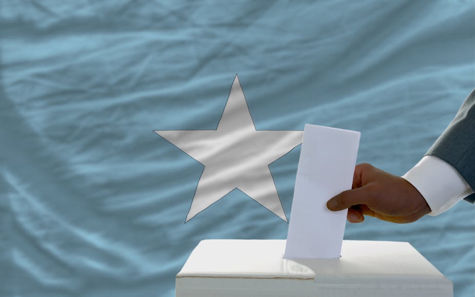 A voter inserts a ballot in a box during elections in front of national flag of Somalia.