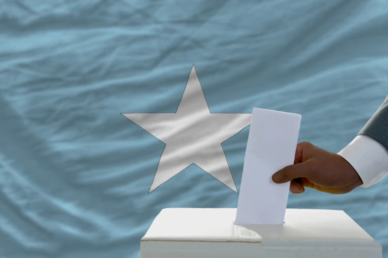 A voter inserts a ballot in a box during elections in front of national flag of Somalia.