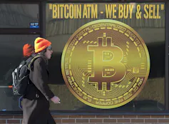 A person walks past a shop that advertises a Bitcoin ATM.