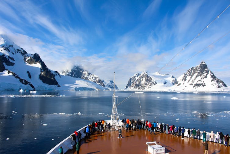 People look out front of boat, icy mountains in background.