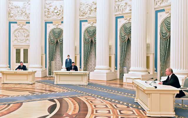 Russian President Putin signs documents in a very grand room.