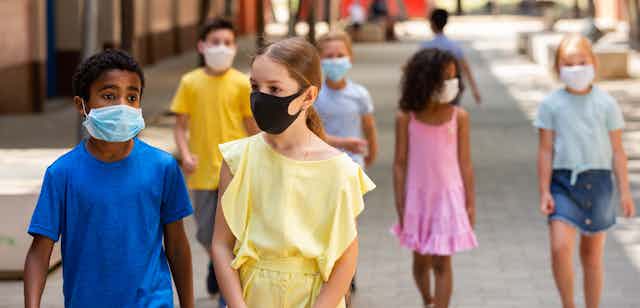 A row of school children walking while wearing face masks
