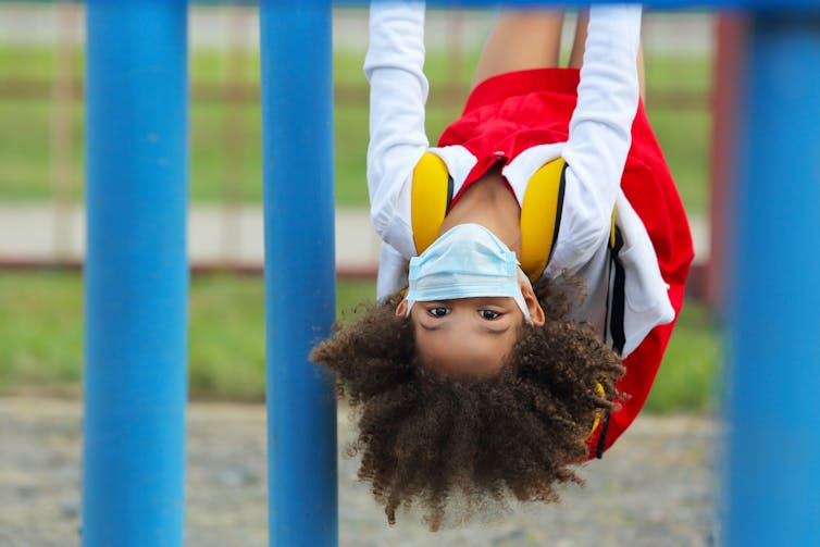 A girl wearing a surgical mask hangs upside down in a swing