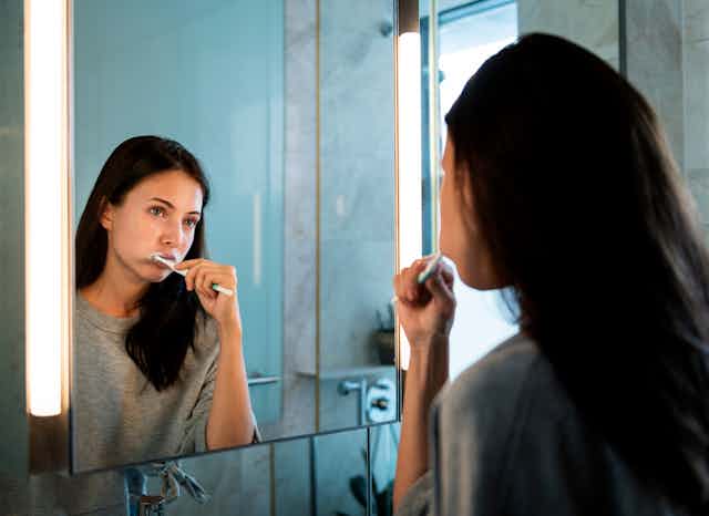 A woman looks in the mirror as she brushes her teeth.