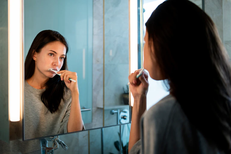 A woman looks in the mirror as she brushes her teeth.