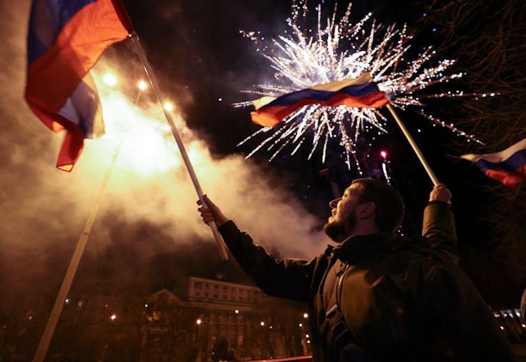 Residents of the breakaway republic of Donetsk in eastern Ukraine wave flags with fireworks in the background.