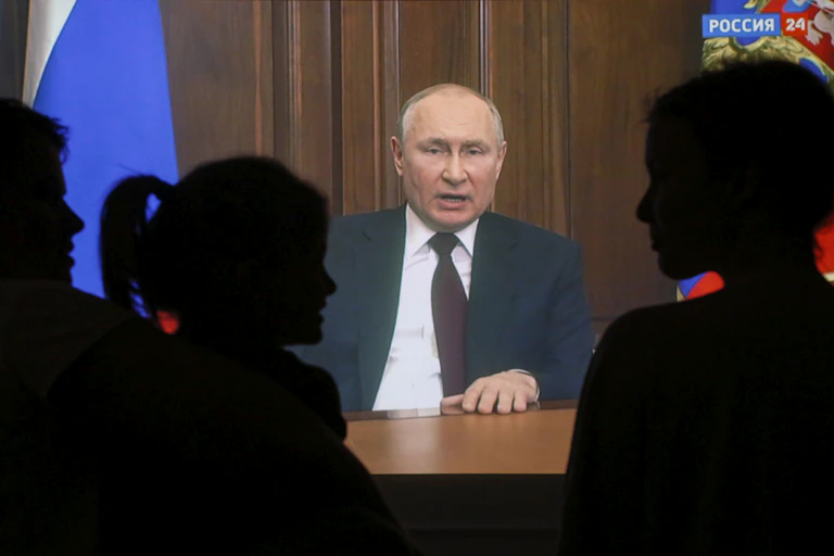 Vladimir Putin makes a televised speech from the Kremlin watched by people shown here in silhouette.