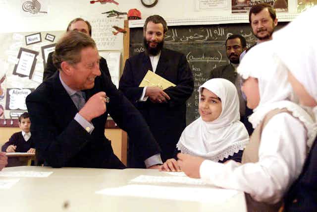 The prince of Wales laughs while talking with school pupils in a classroom.