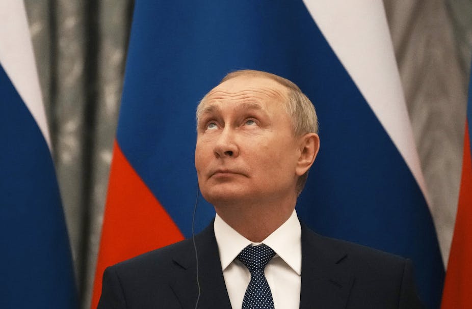 Vladimir Putin gazes upwards, with a Russian flag behind him