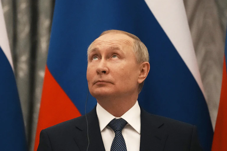 Vladimir Putin gazes upwards, with a Russian flag behind him