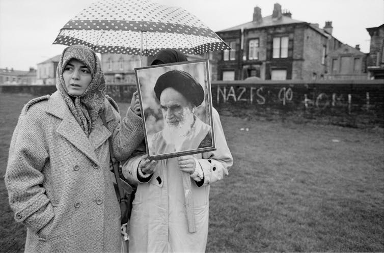 Protesters hold up images of Ayatollah Khomeini in a field in the rain.