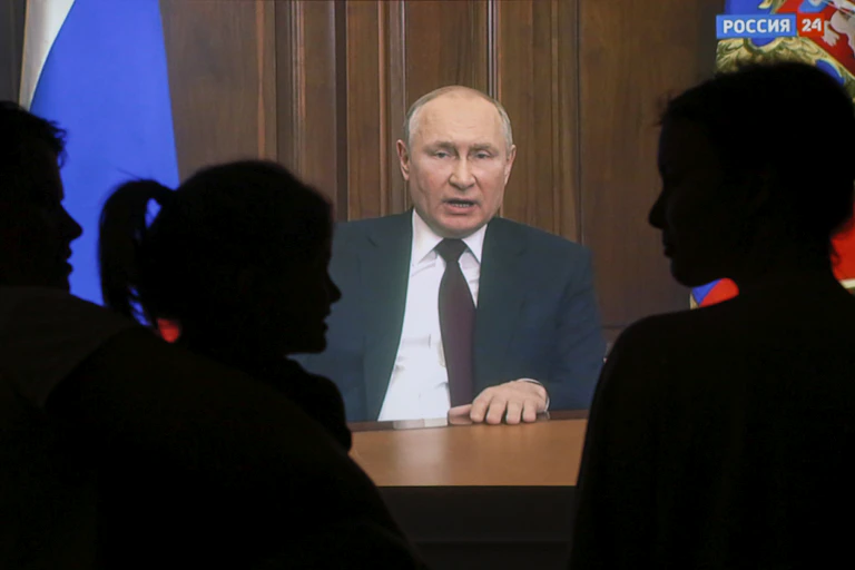 Vladimir Putin pronuncia un discurso televisado desde el Kremlin, observado por personas que aparecen aquí en silueta.