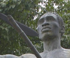 Statue of a man looking up holding a pole.