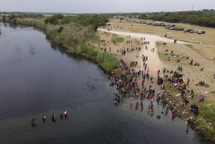 Migrants seen crossing a river in aerial view.