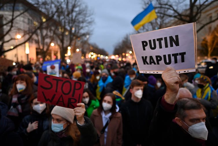 Hundreds of people demonstrate, holding protest signs such as Stop War! and Putin Kaputt.