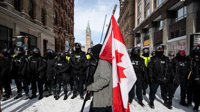 A protester carries a canadian flag as he walks past a line of police with the peace tower in the background