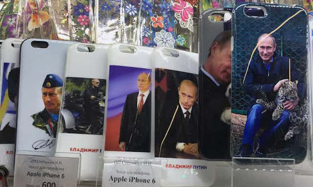 Cell phone covers show varying photos of Vladimir Putin, including one of him holding a small cheetah