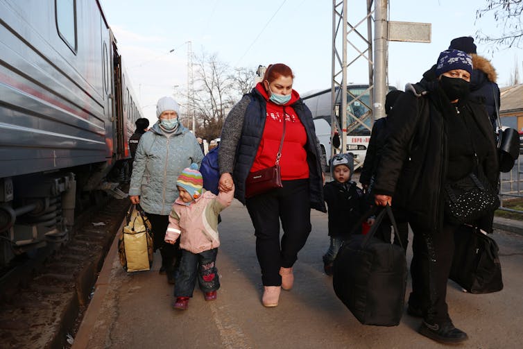 A group of people holding luggage are seen walking away from a train.