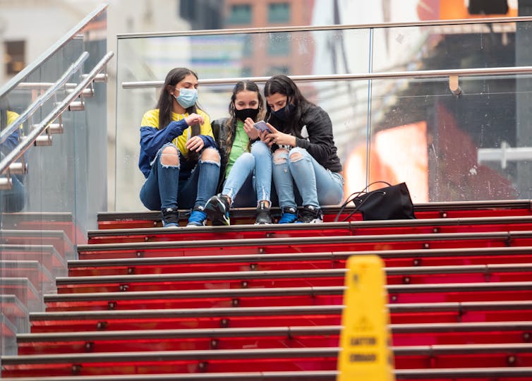 Three people sit on stairs outside and use their smartphones
