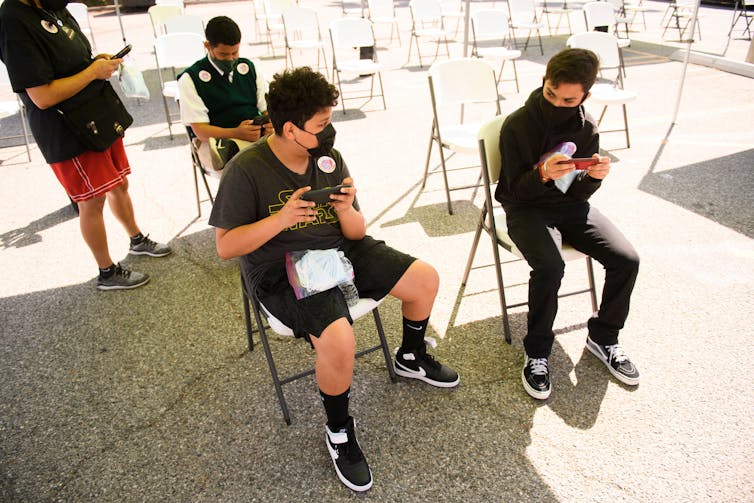 Two young people sit on folding chairs and look at their phones