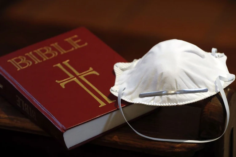 A Bible next to a disposable face mask.