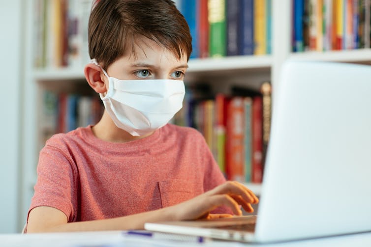 Boy in a masks works at a computer.