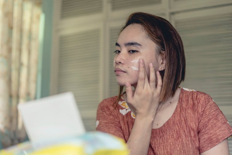 A woman applies sunscreen at home.