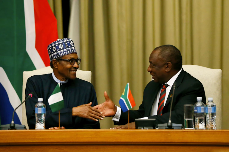A man dressed in African traditional wears stretching hands to greet another man dressed in a grey suit