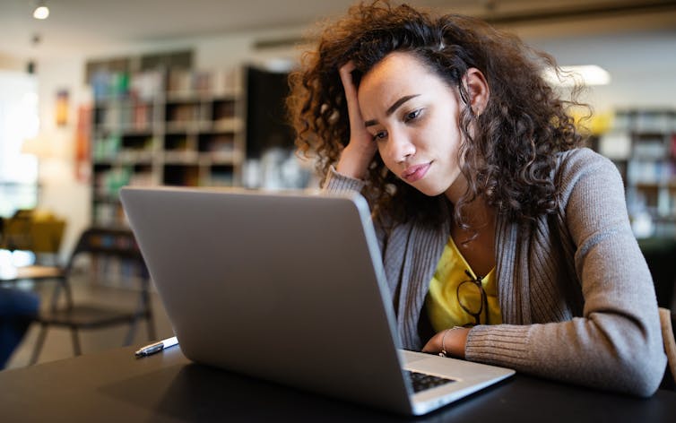A woman sitting at a laptop, looks stressed.
