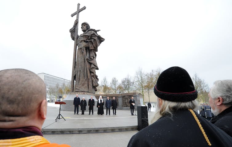 A woman photographs Vladimir Putin and other dignitaries standing by a statue of Vladimir the Great in Moscow.