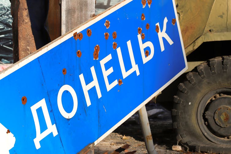 A blue sign marked by bullet holes that reads 'Donetsk' in Ukrainian