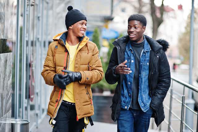 Two young Black men in winter coats in an outdoor setting, smiling.