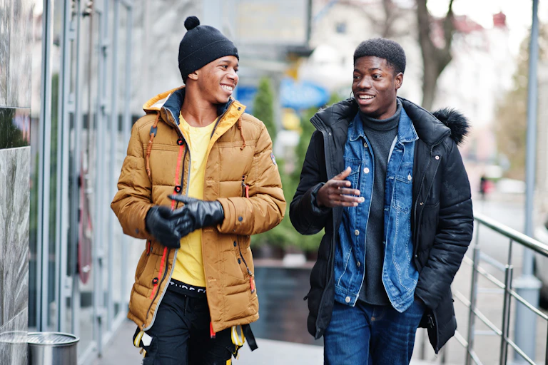 Two young Black men in winter coats in an outdoor setting, smiling.