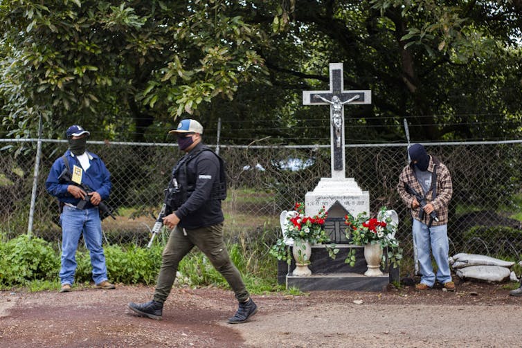 Three men with guns in front of an orchard.