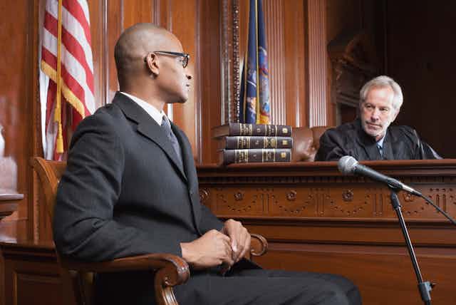 A judge skeptically looks at a man seated opposite his bench.
