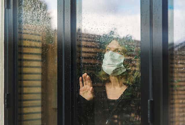 A senior woman, in isolation at home, looks out a window.